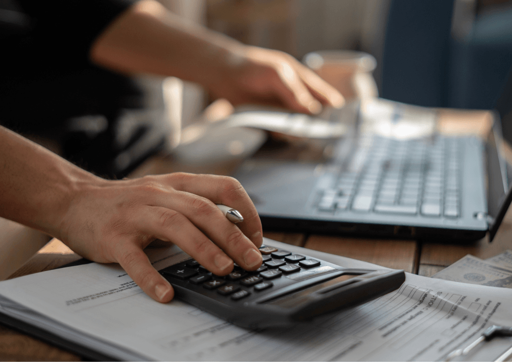 A person calculating on a laptop, focused on the screen while using a calculator for assistance with numbers.